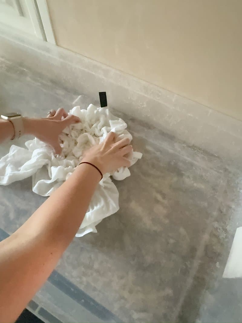 Hands scrunching white fabric into crumple pattern on marble counter